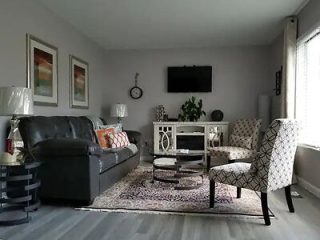 A stylish living room with a black leather couch, patterned armchairs, and a soft rug, creating a modern yet homey space.